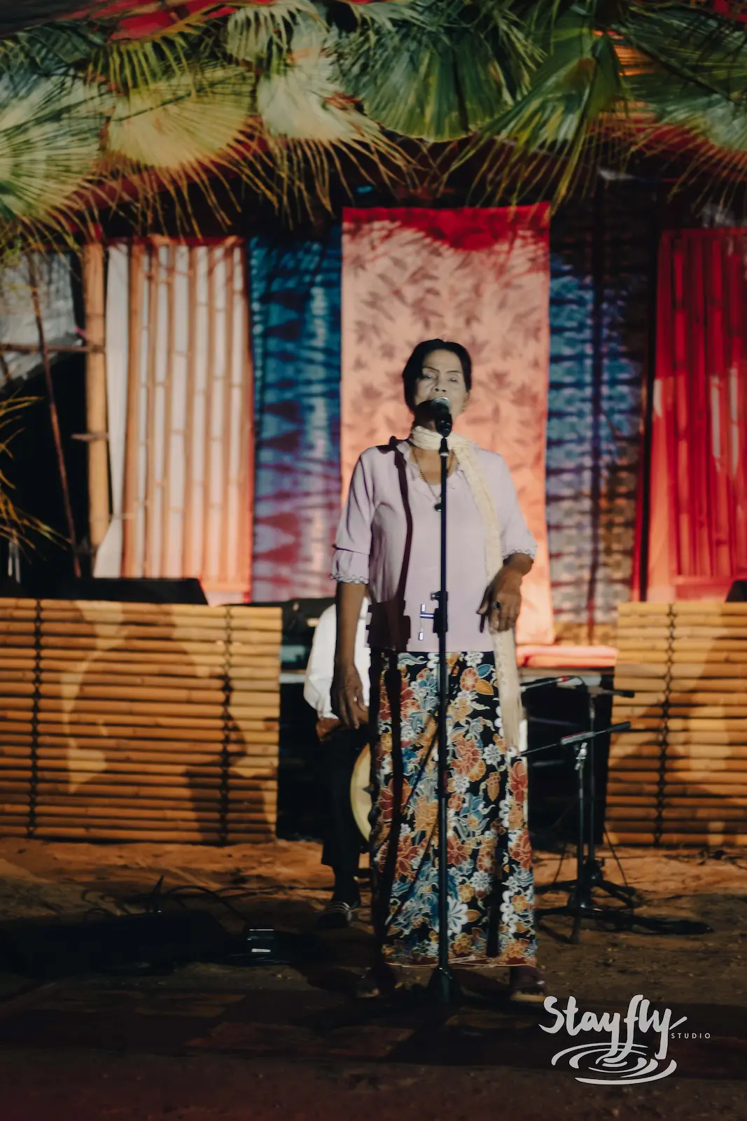 Woman singing on stage with patterned backdrop.