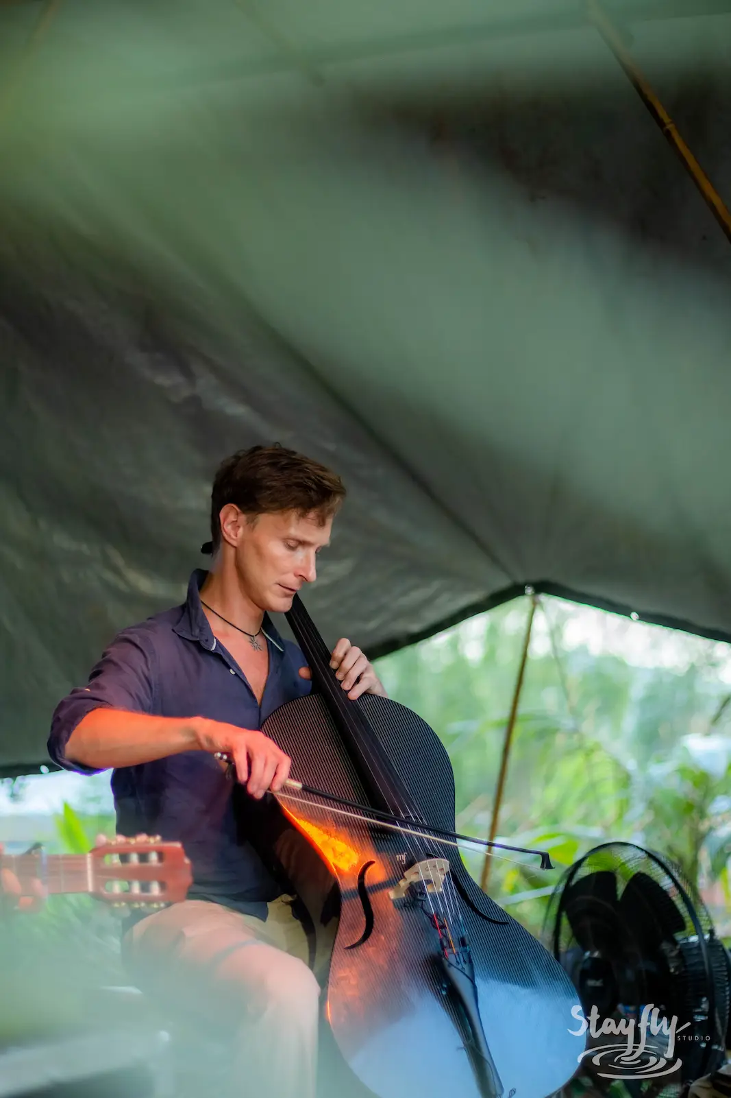 Man playing cello under a tent.
