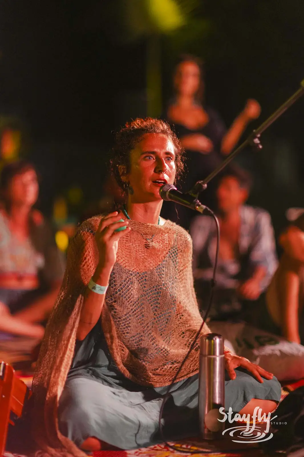 Woman singing seated cross-legged at night.