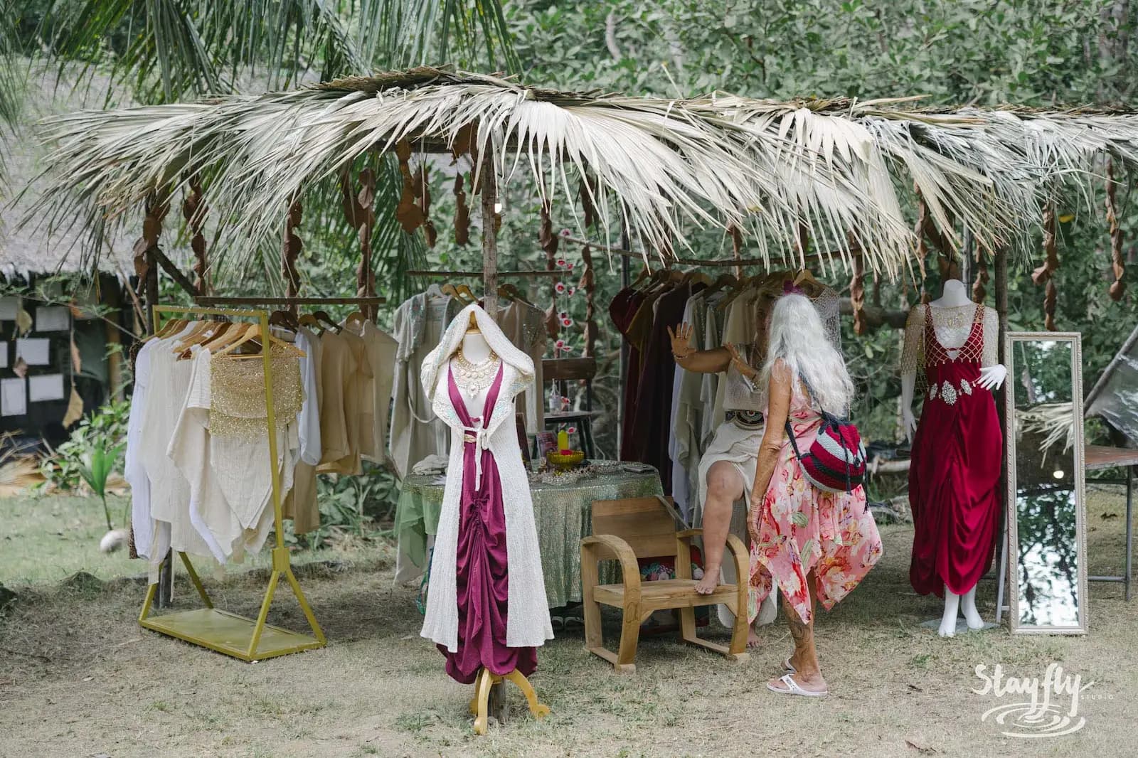 Woman browsing clothing rack under thatched market stall.