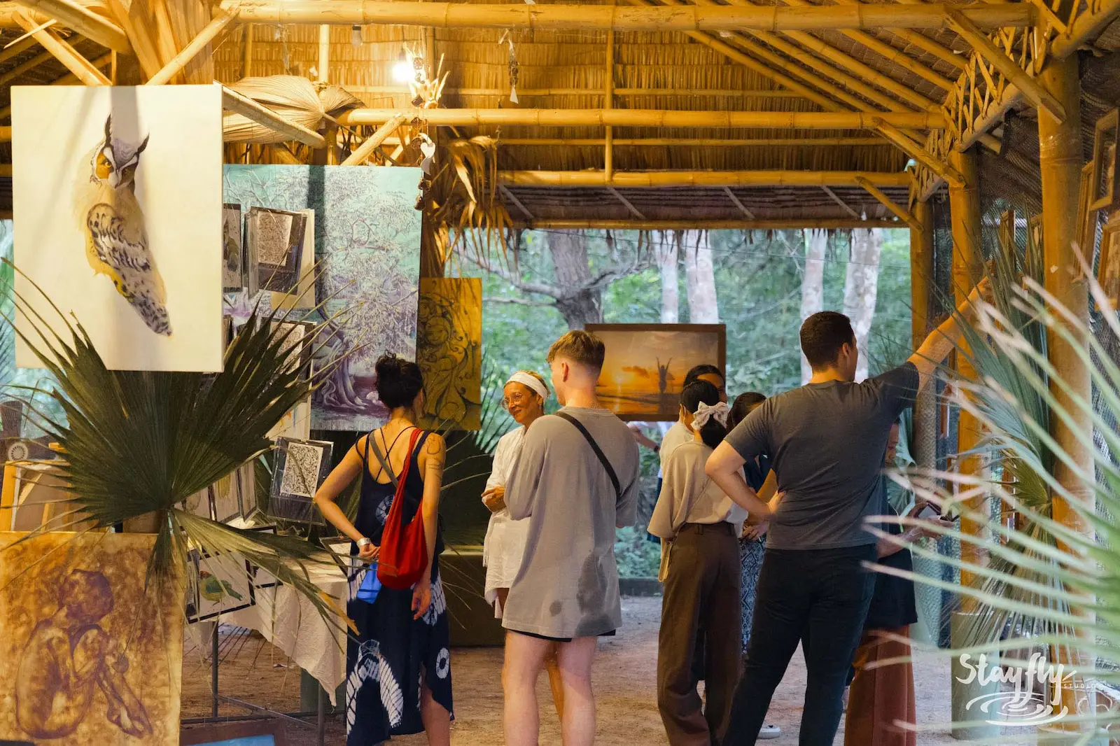 Visitors browsing framed artwork in bamboo gallery hall.