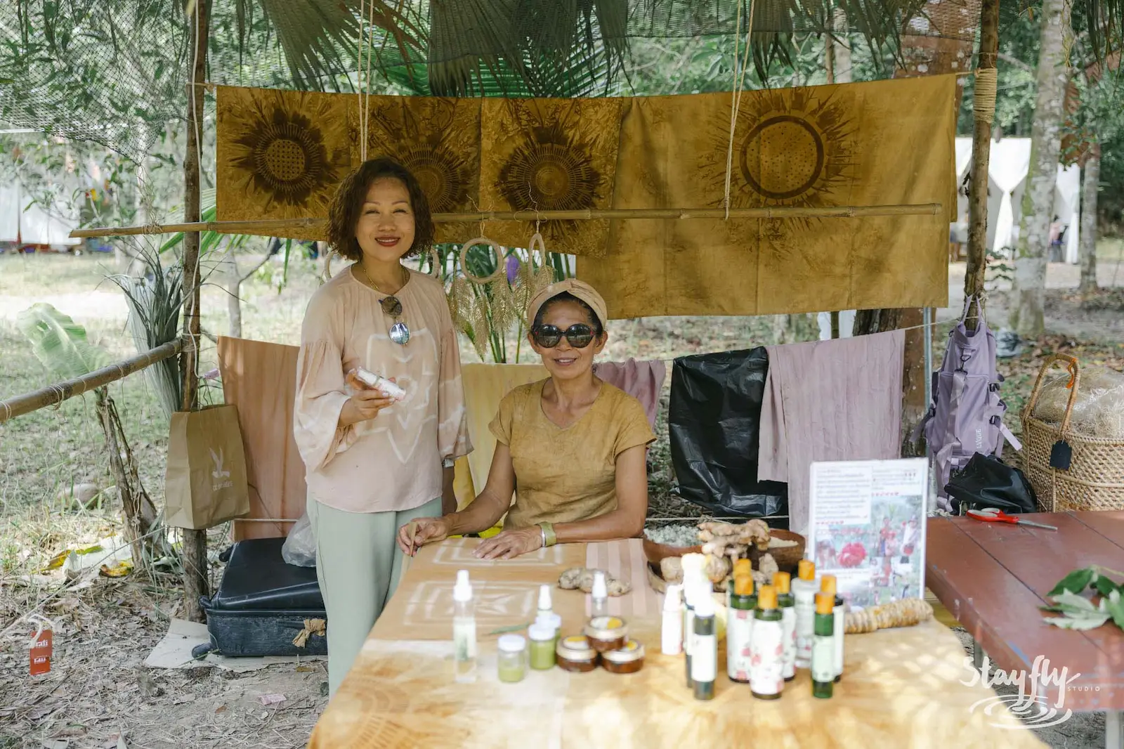 Two women posing at skincare and textile craft stall.