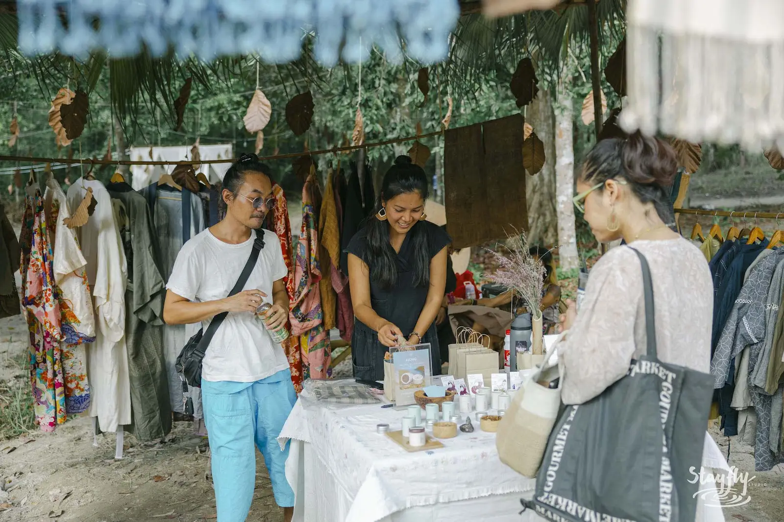Shoppers browsing clothing rack at market stall.
