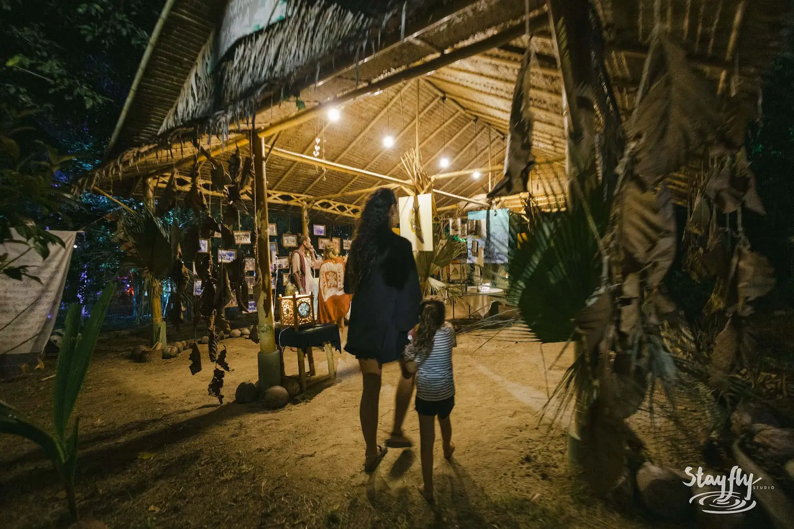 Woman and child walking past lit market booth at night.