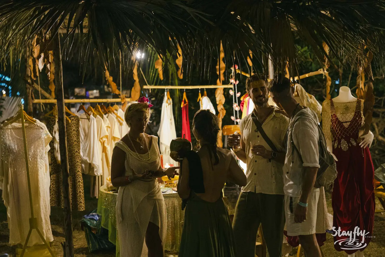 Visitors browsing clothing stall lit at night.