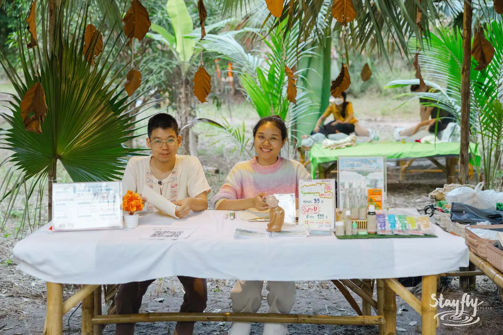 Two vendors smiling at decorated market info table.