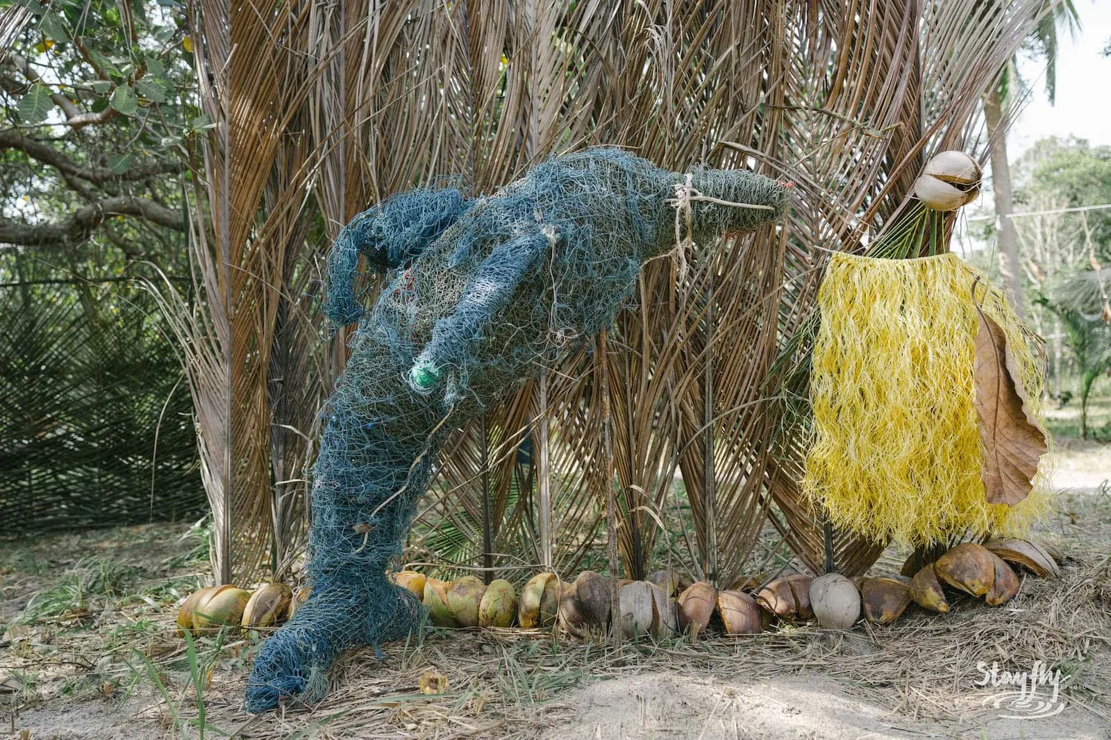 Woven blue fiber sculpture displayed among palm fronds.