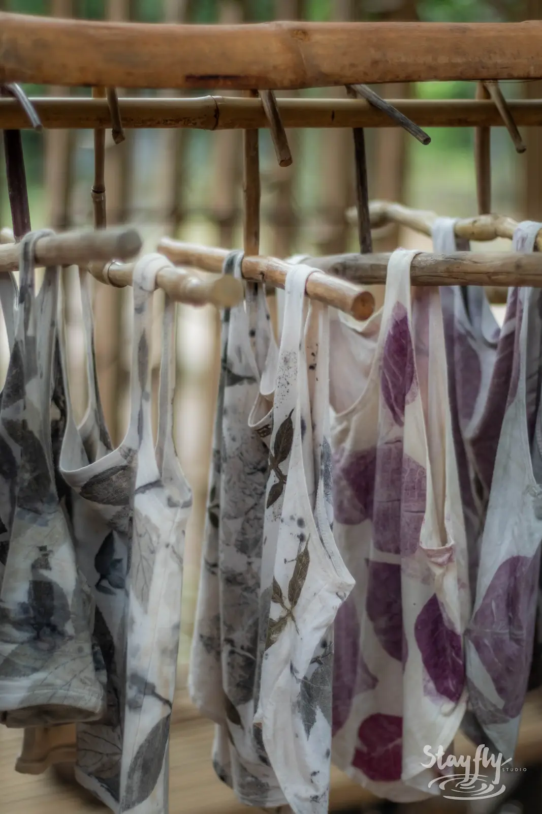 Eco-printed tank tops hanging on wooden rack.