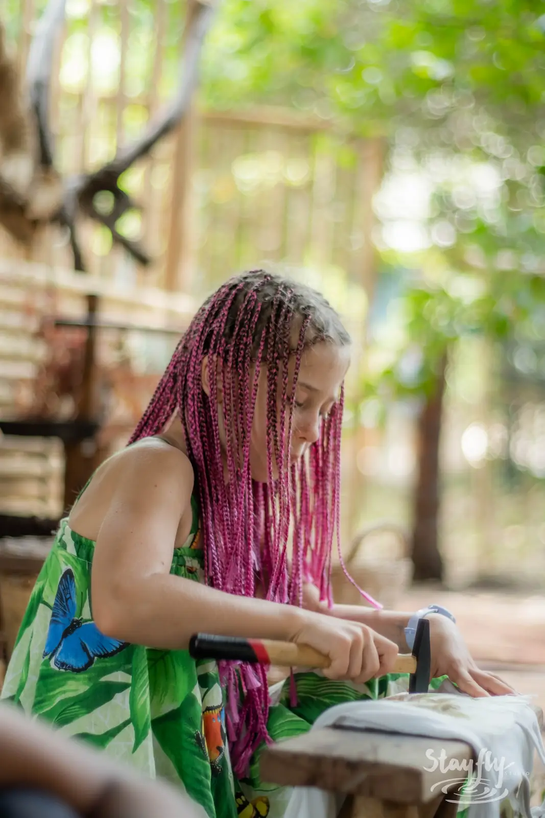 Girl with pink braids carving wood at a stall.