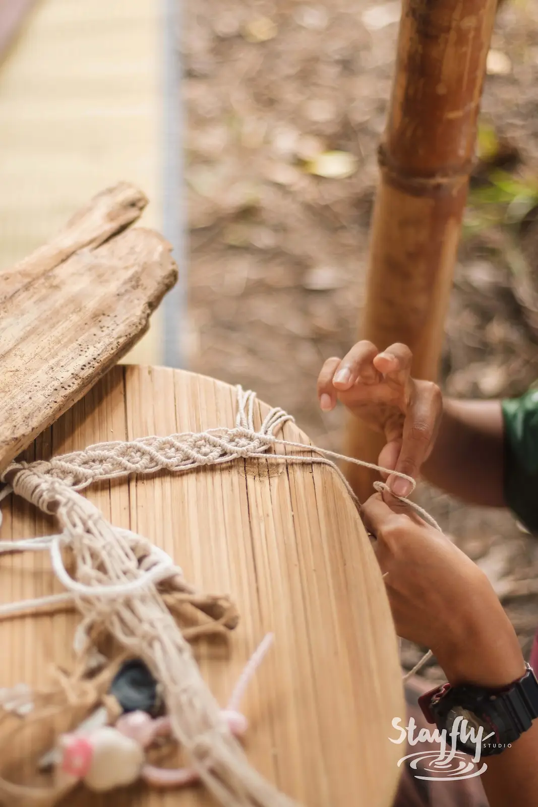 Hands weaving macrame bracelet on wooden loom.