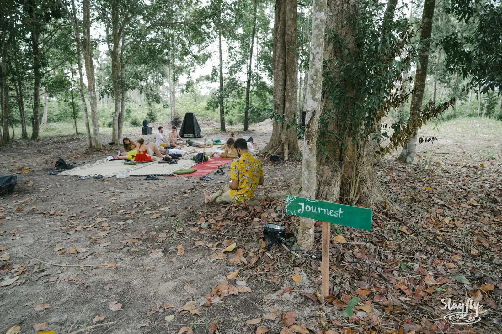 Journest sign, group seated on mats under trees.