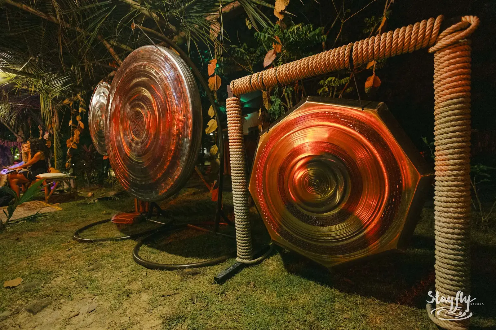 Large gong instruments lit orange outdoors at night.