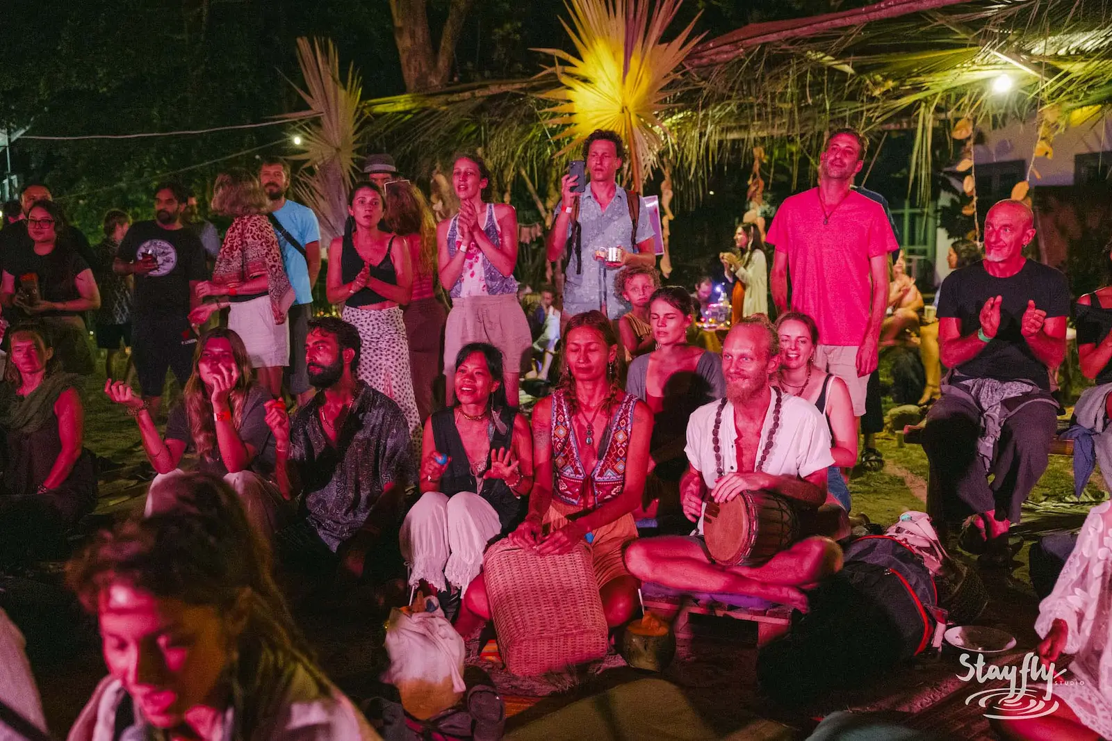 Night crowd watching drummer at forest gathering.