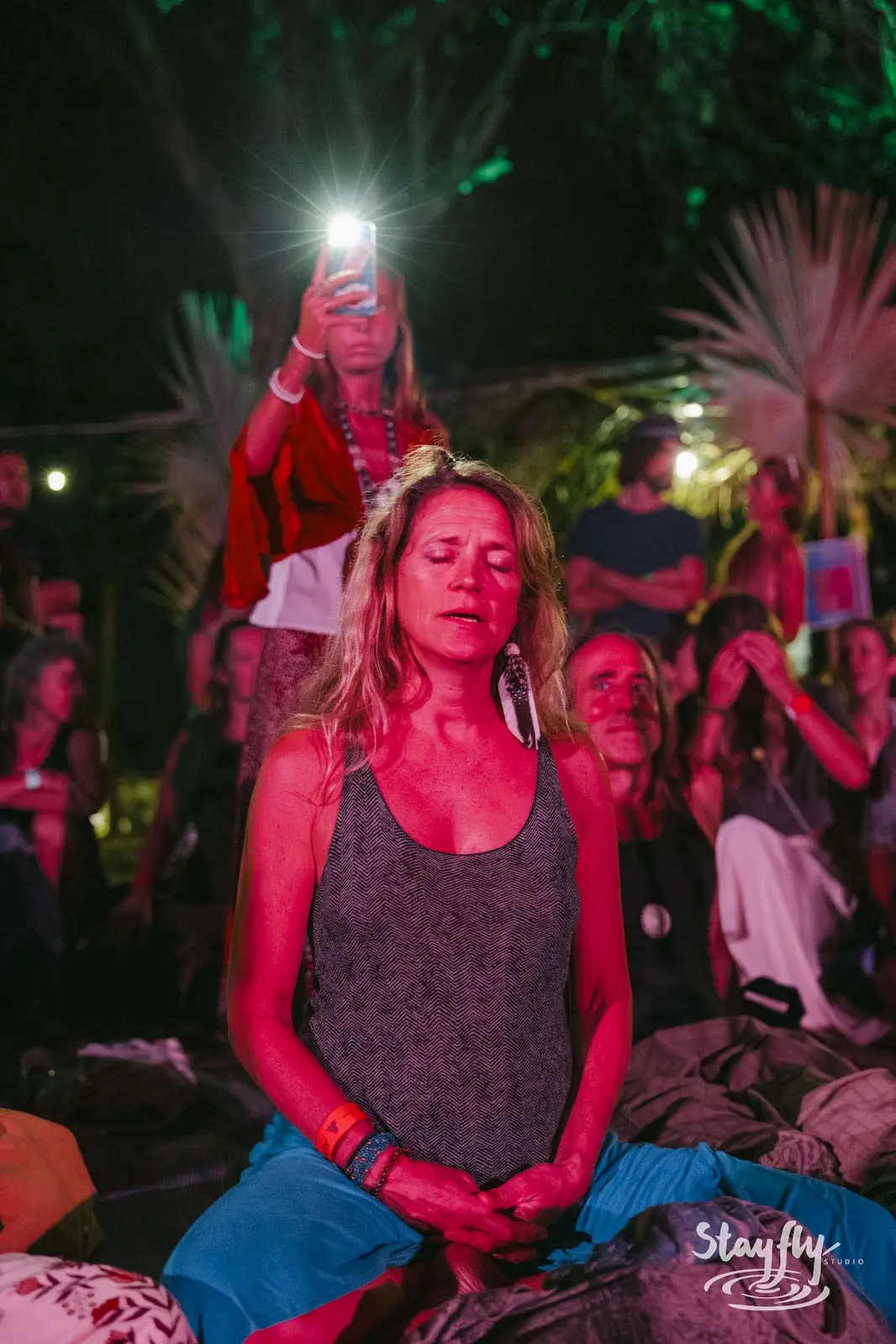 Woman meditating at night, phone light behind her.