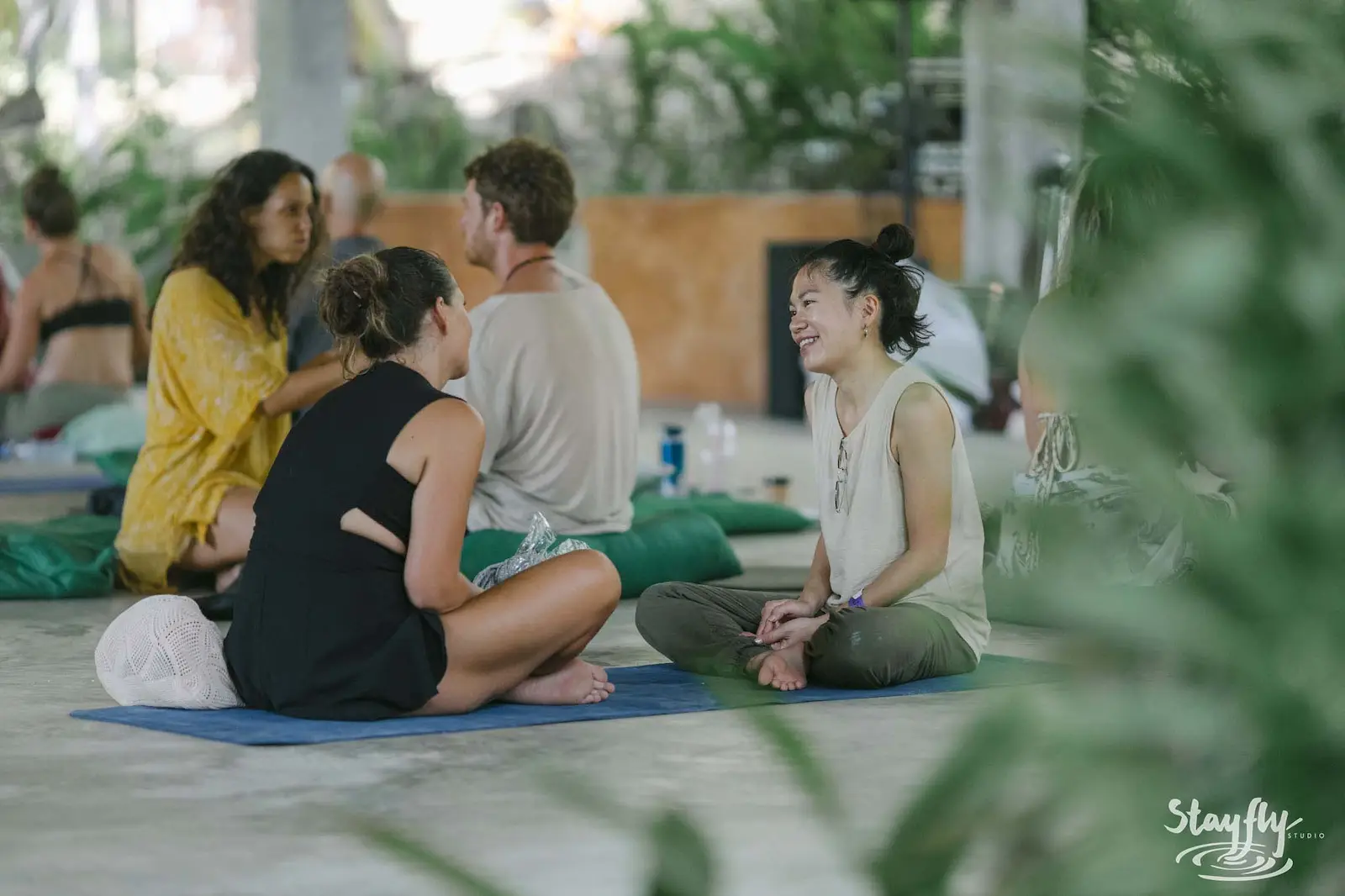 Group seated on mats laughing in open-sided hall.