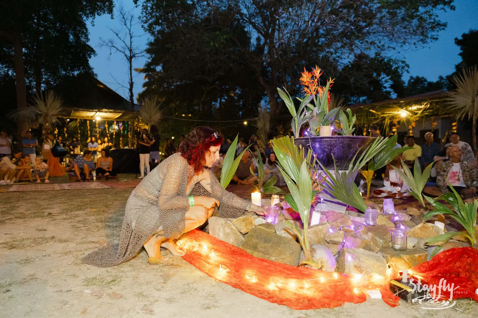 Woman kneeling at candlelit altar installation at night.