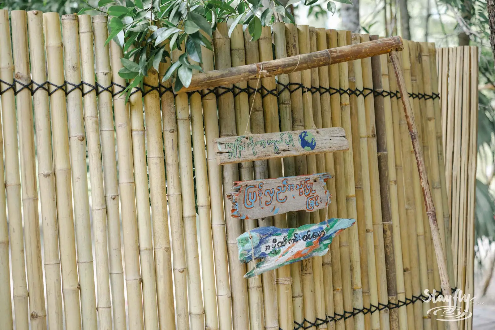 Hand-painted wooden signs hang on bamboo fence.