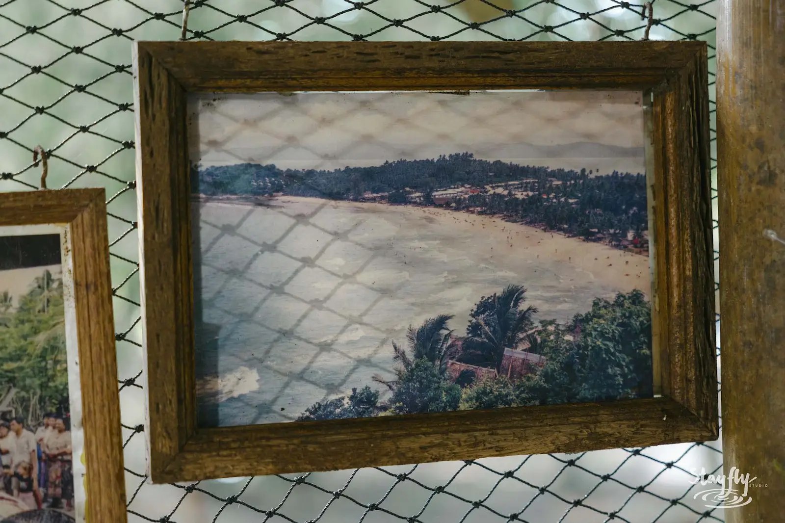 Framed vintage coastal photo hung on netting wall.
