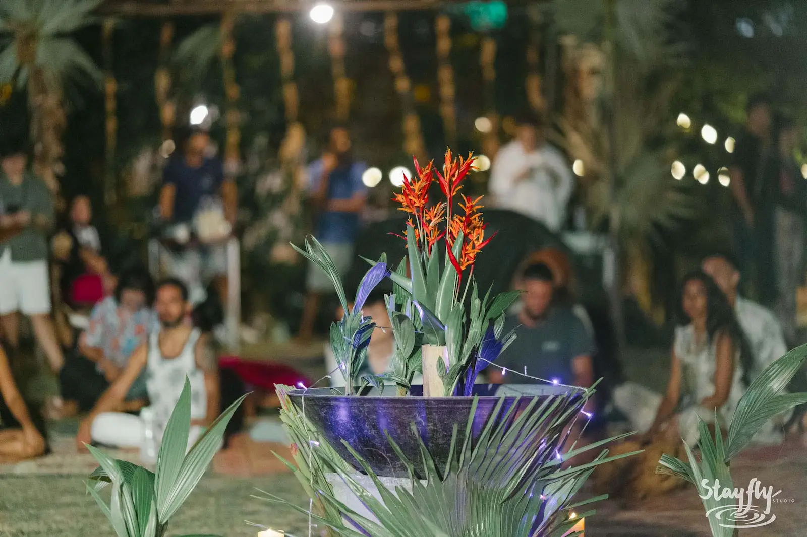 Red flower arrangement in vase, crowd blurred behind.