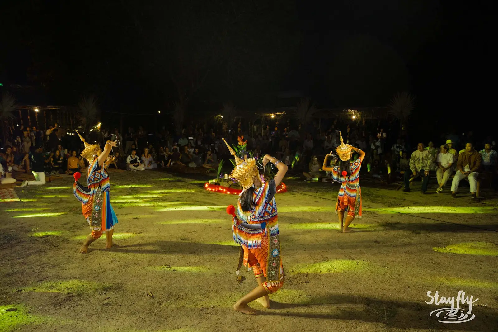 Three masked dancers performing before seated crowd.