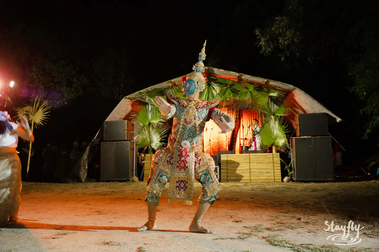 Elaborately costumed dancer performing before decorated stage.