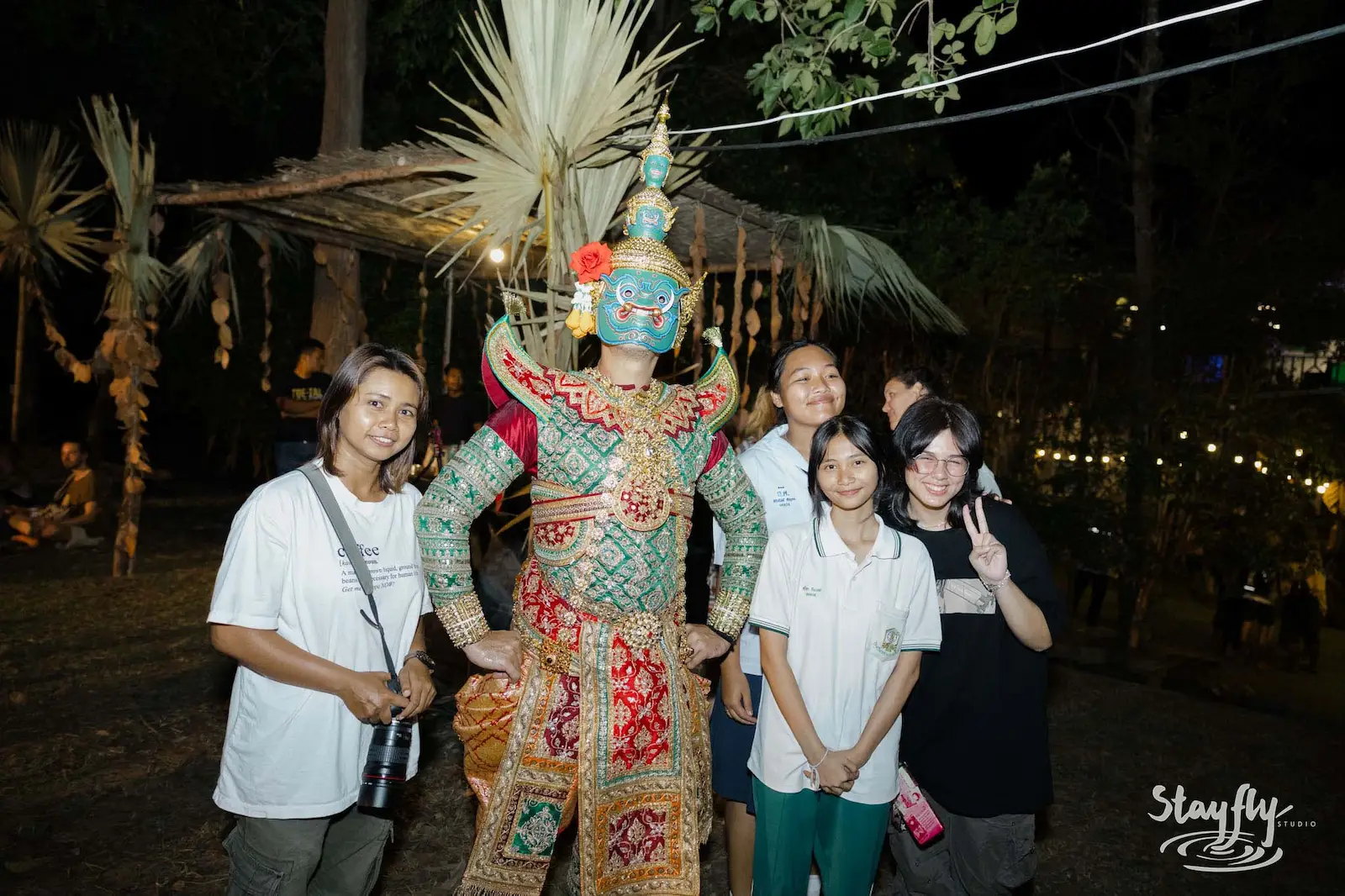 Visitors posing with masked khon dancer at night.