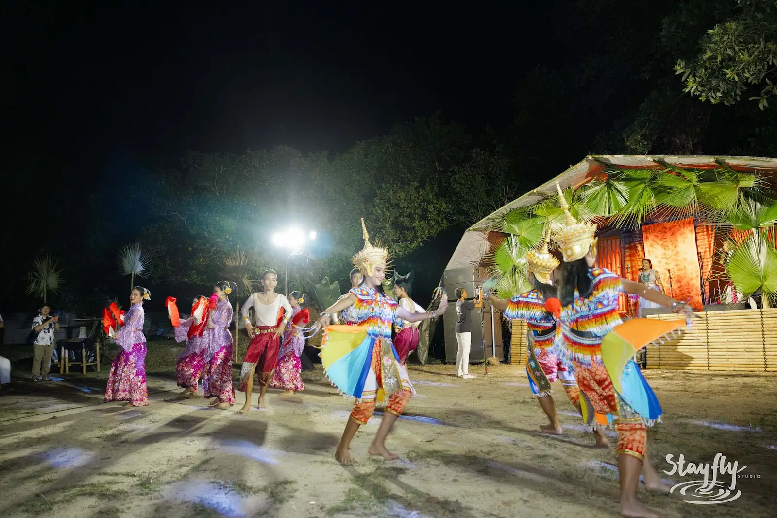 Dance troupe with fans and headdresses performs outdoors.