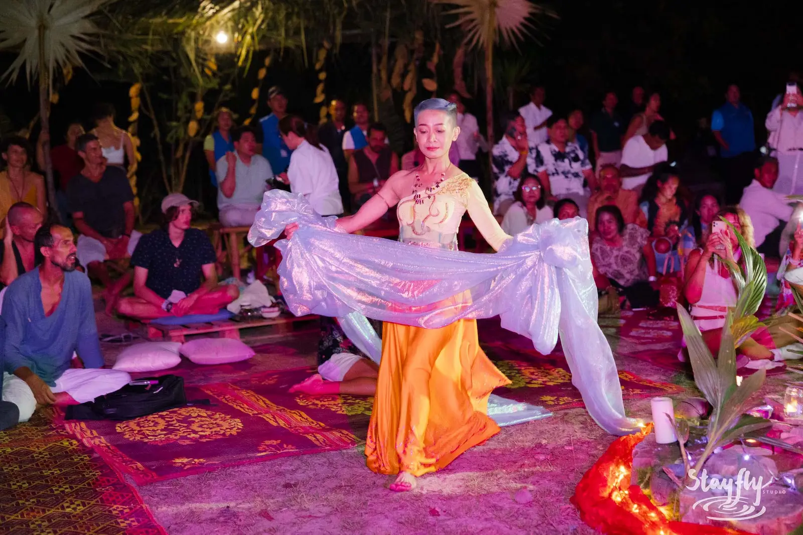 Dancer in orange dress swings white shawl for crowd.
