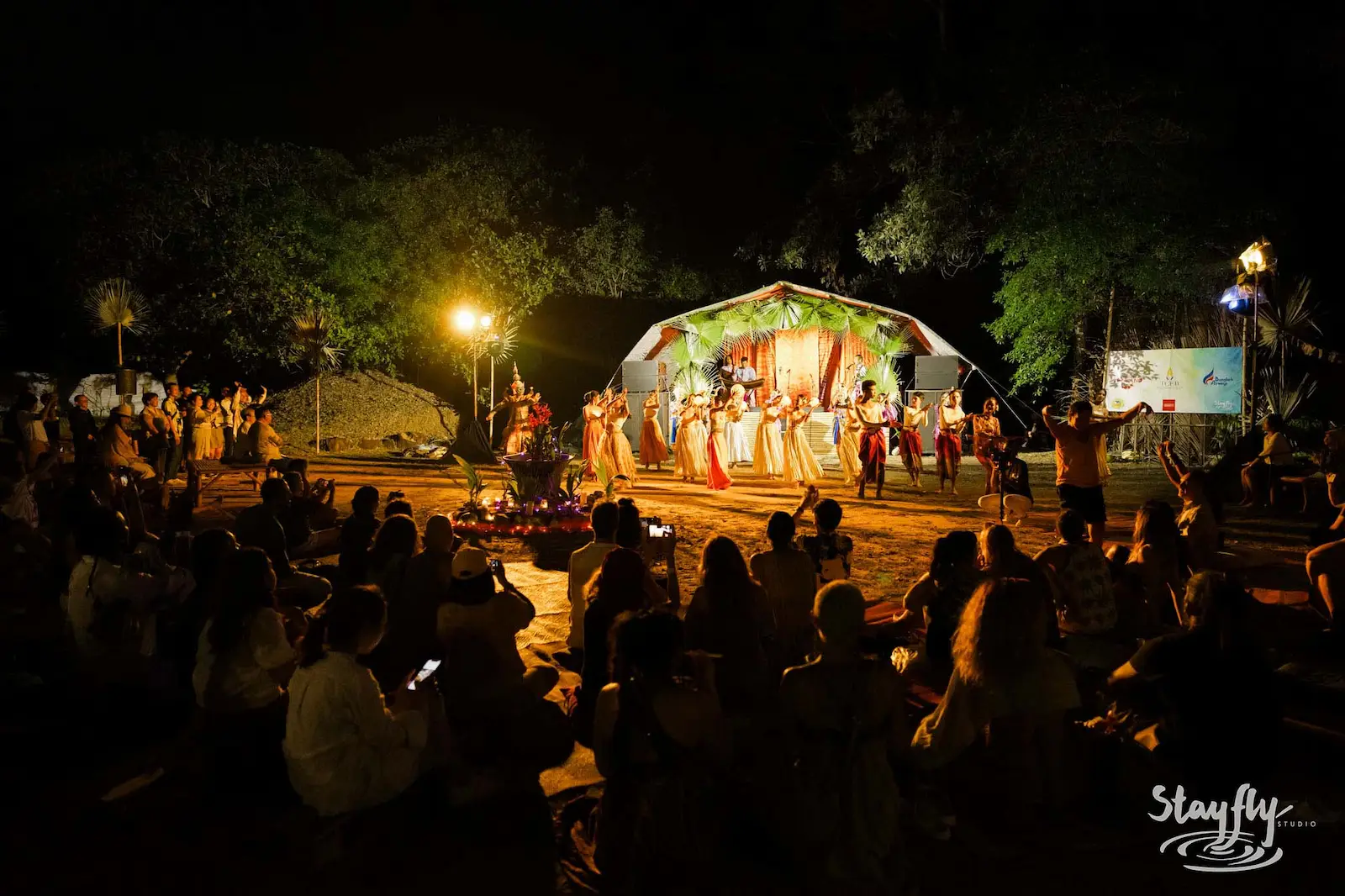 Costumed dance performance watched by seated crowd at night.