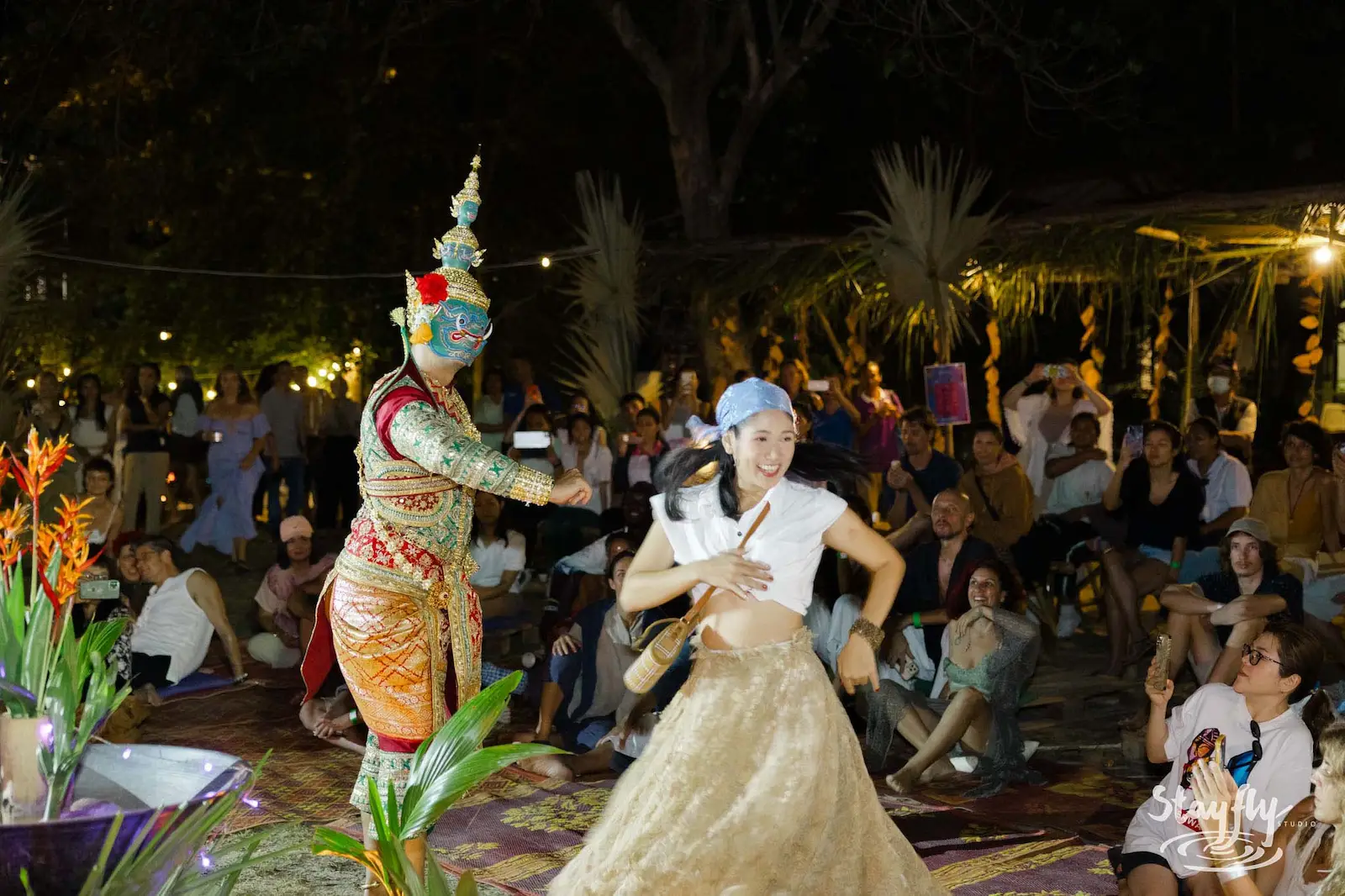 Khon dancer performing with dancer in white before crowd.