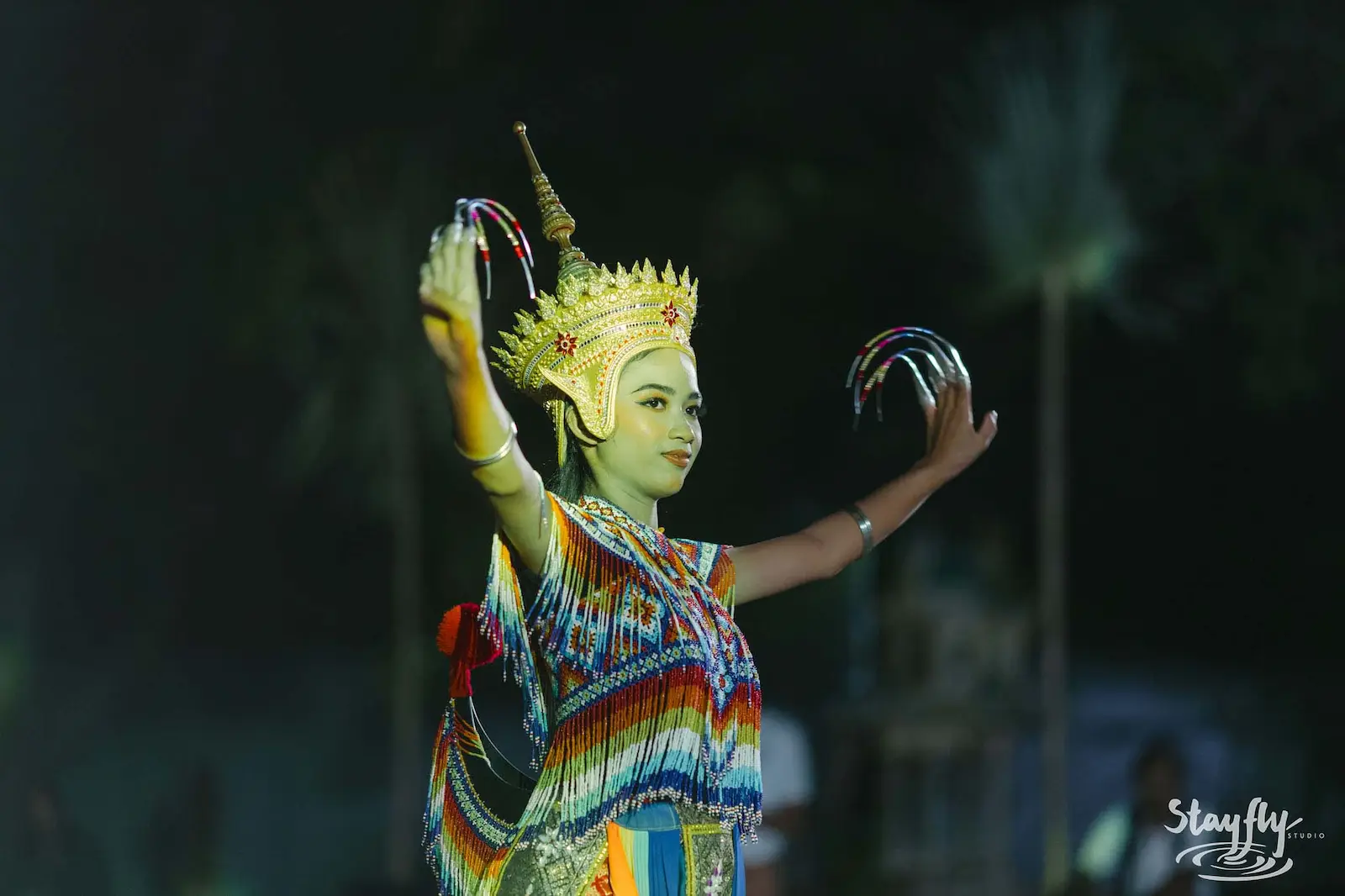 Costumed dancer with gold headdress performing at night.