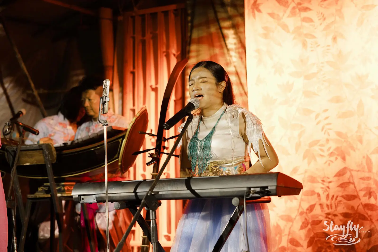 Young singer at keyboard on decorated stage.