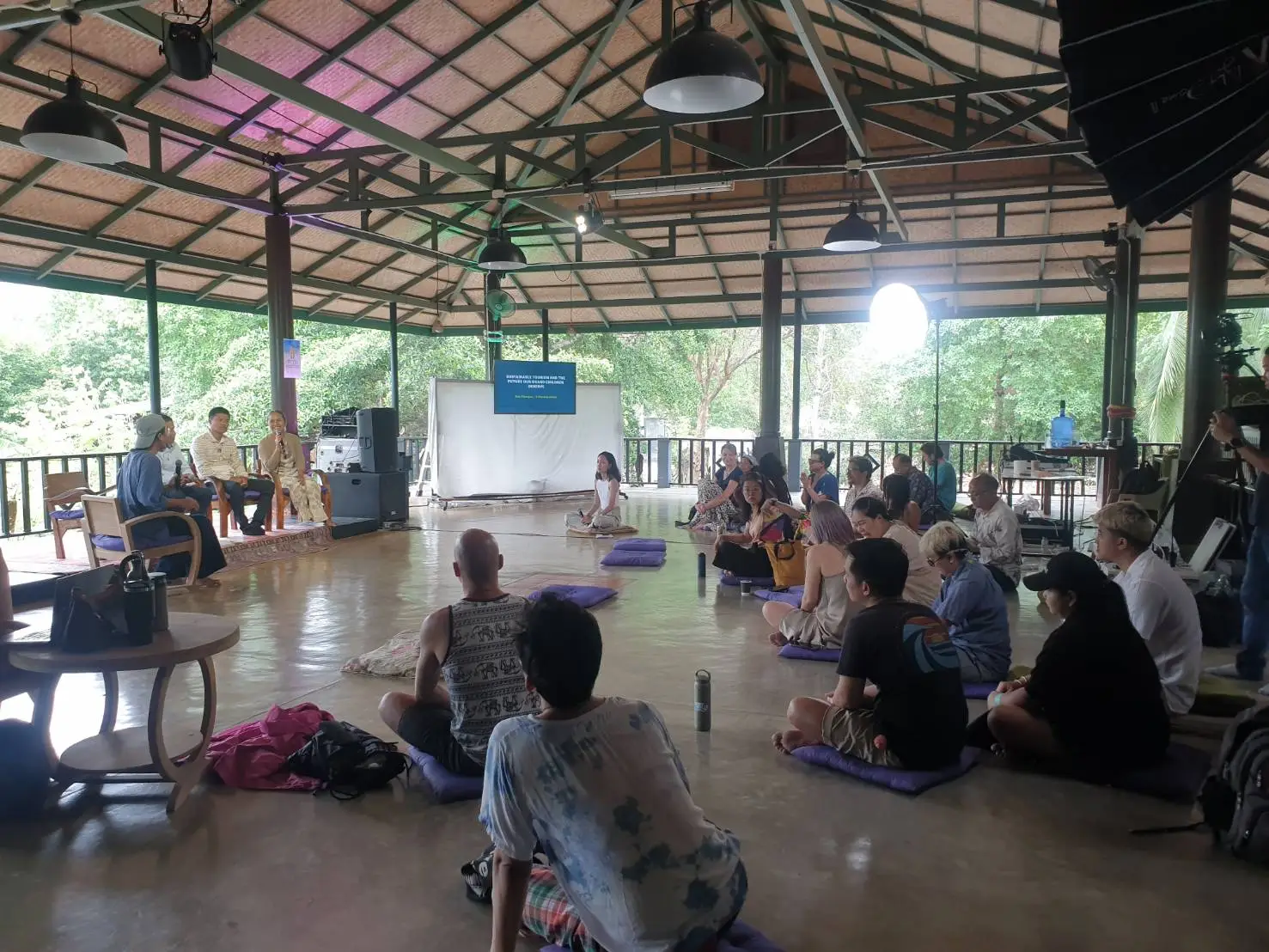 Seated audience at forum talk under open hall.