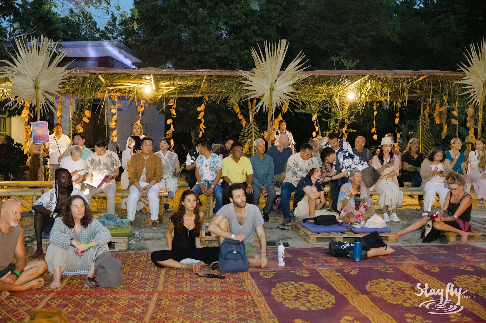 Seated evening audience under decorated canopy.
