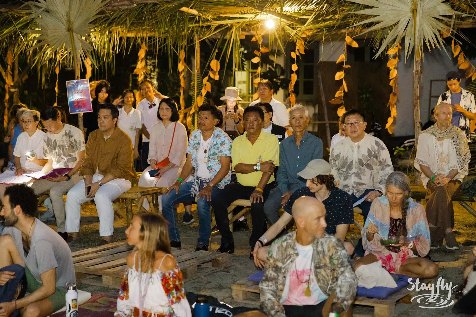 Mixed-age audience seated listening at outdoor forum.