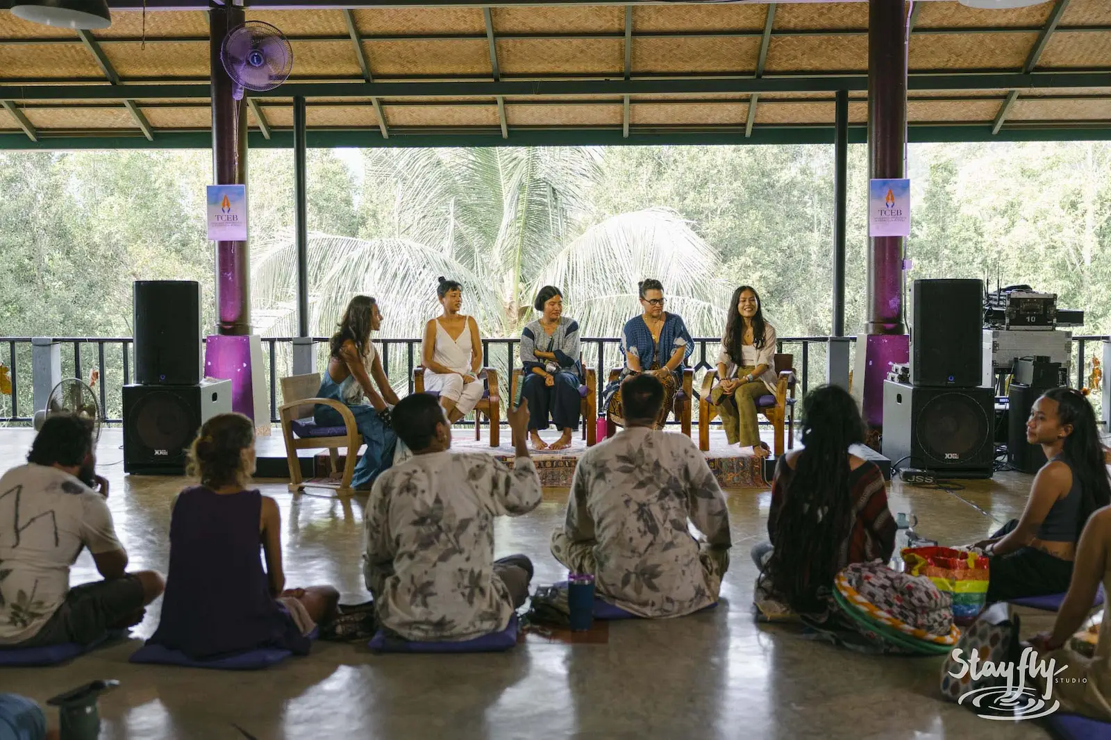 Panel of five seated speakers facing circle audience.