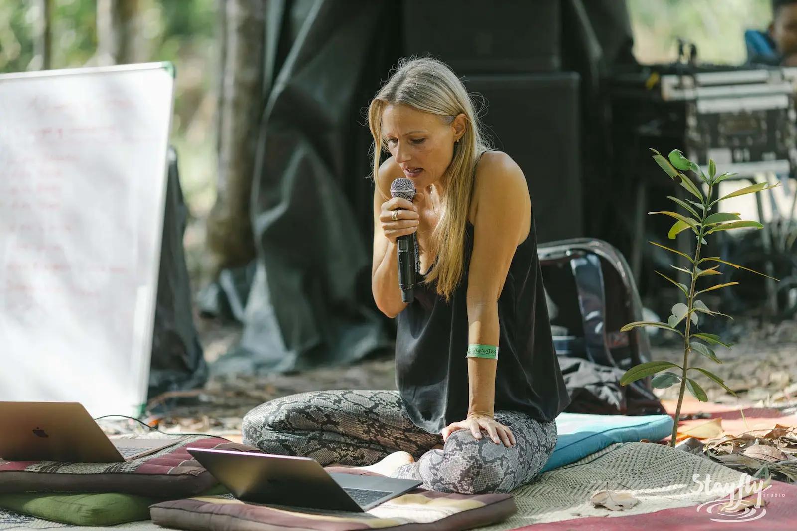 Woman speaking into microphone seated outdoors with laptop.