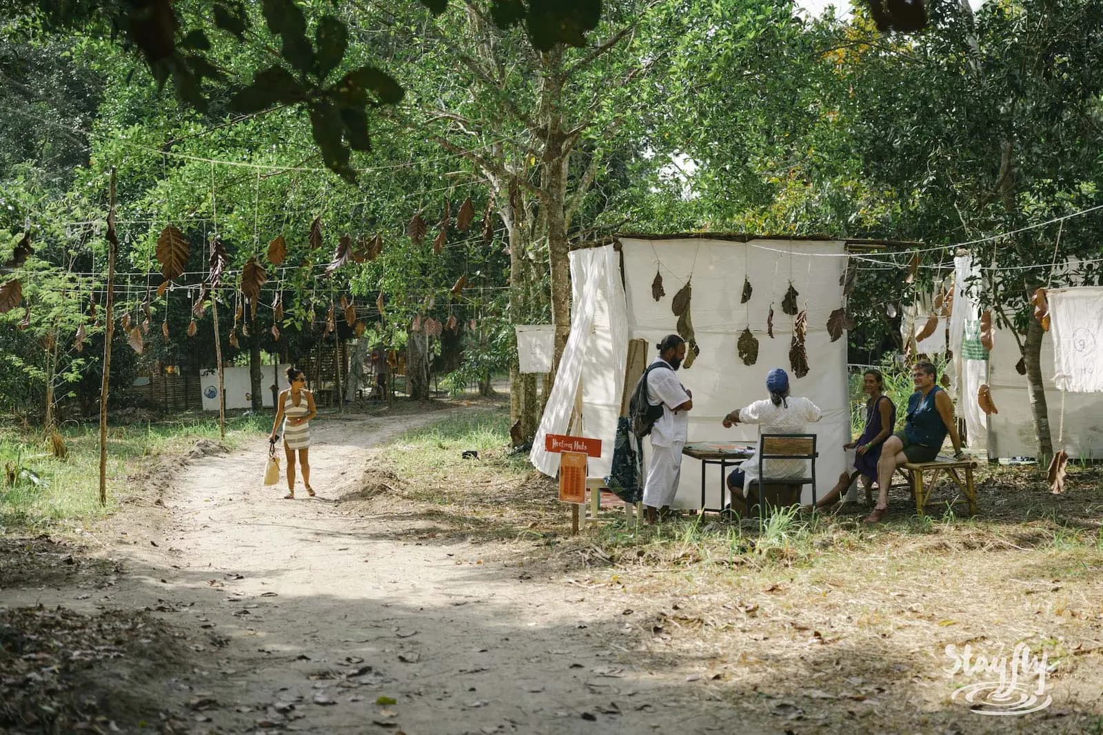 Forest path past healing huts with seated people.