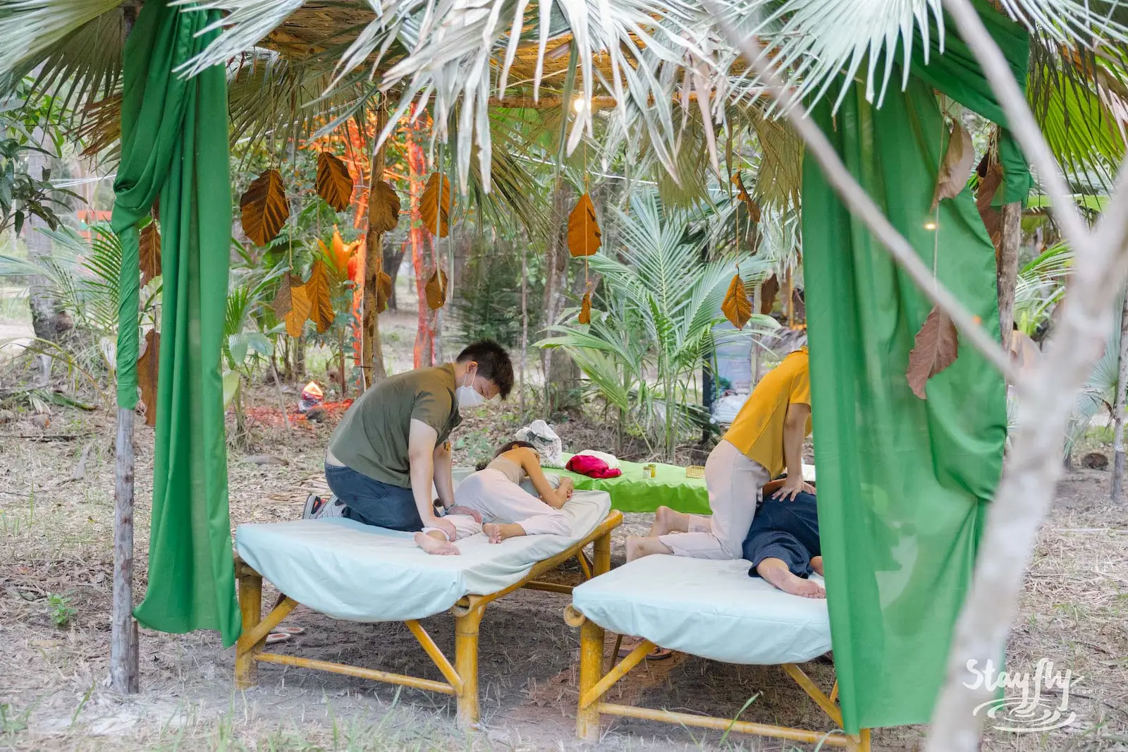 Two masseuses working on clients under green canopy.