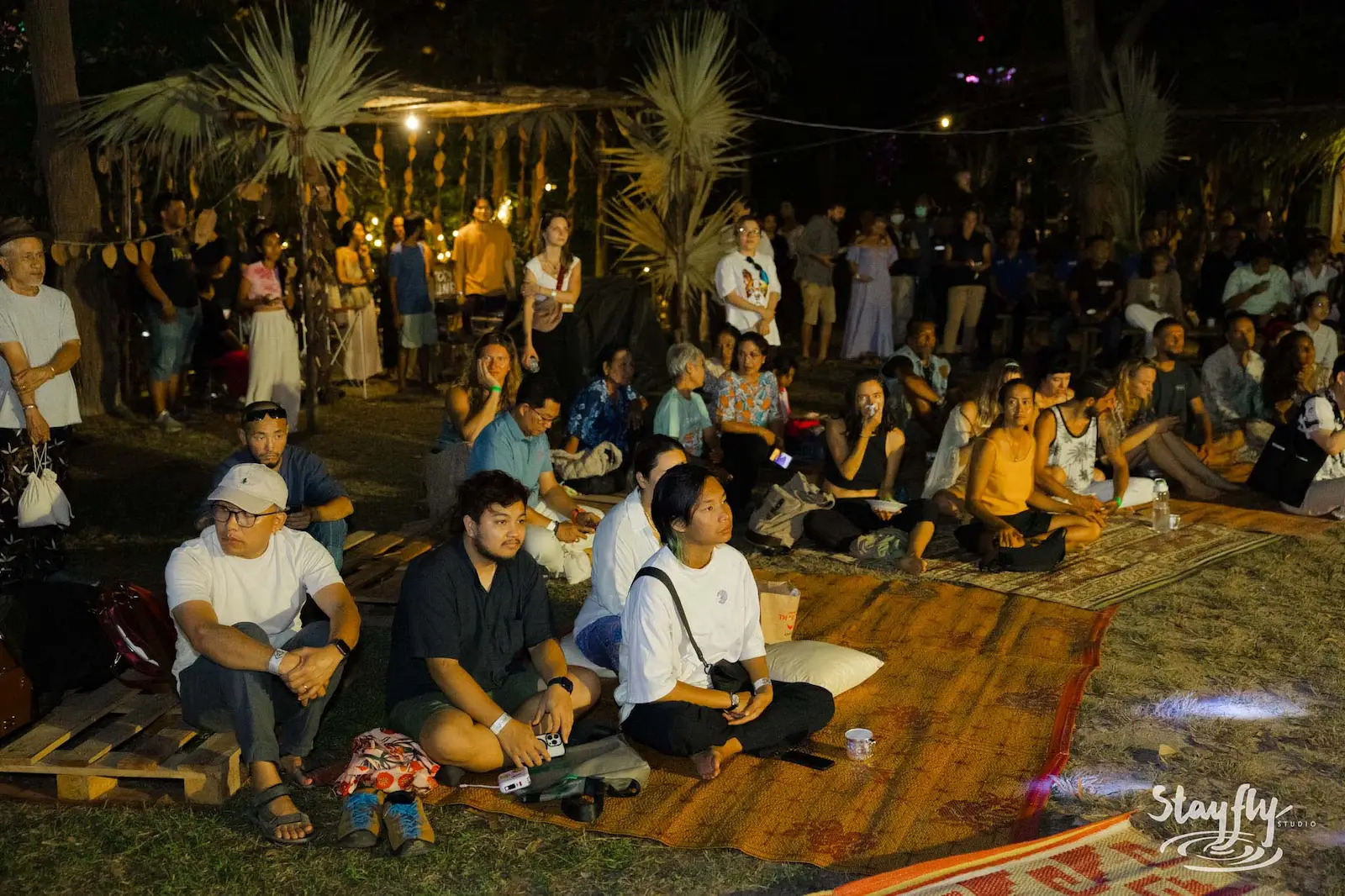 Crowd seated on mats at night ceremony gathering.
