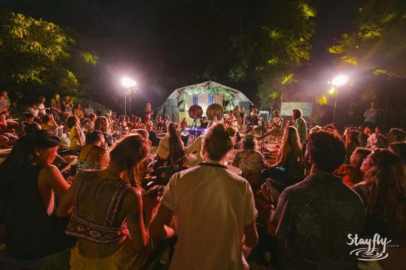 Crowd faces lit dome-tent stage at night.