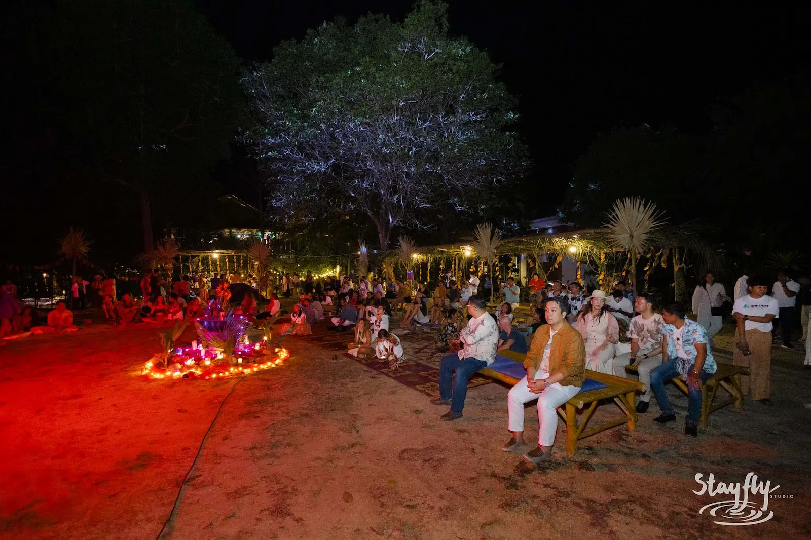Crowd seated on benches beside flower-lit fire pit.