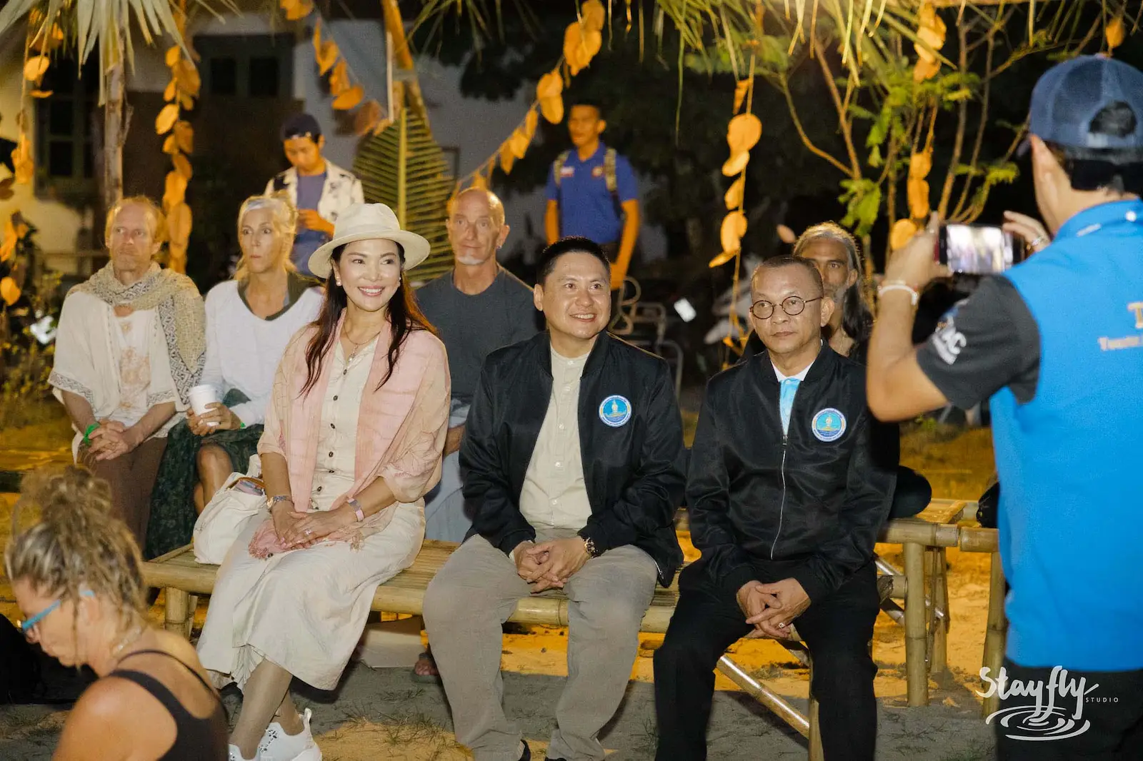 Seated officials in jackets being photographed at night event.