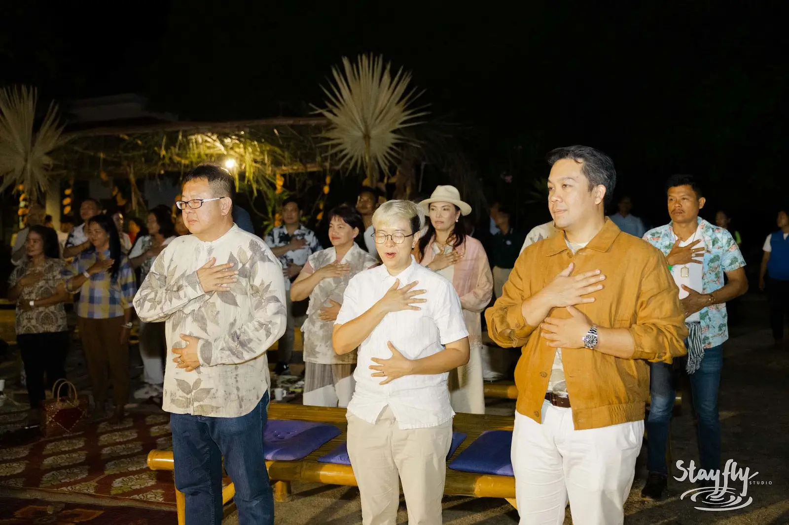 Group standing with hands on chest at night ceremony.