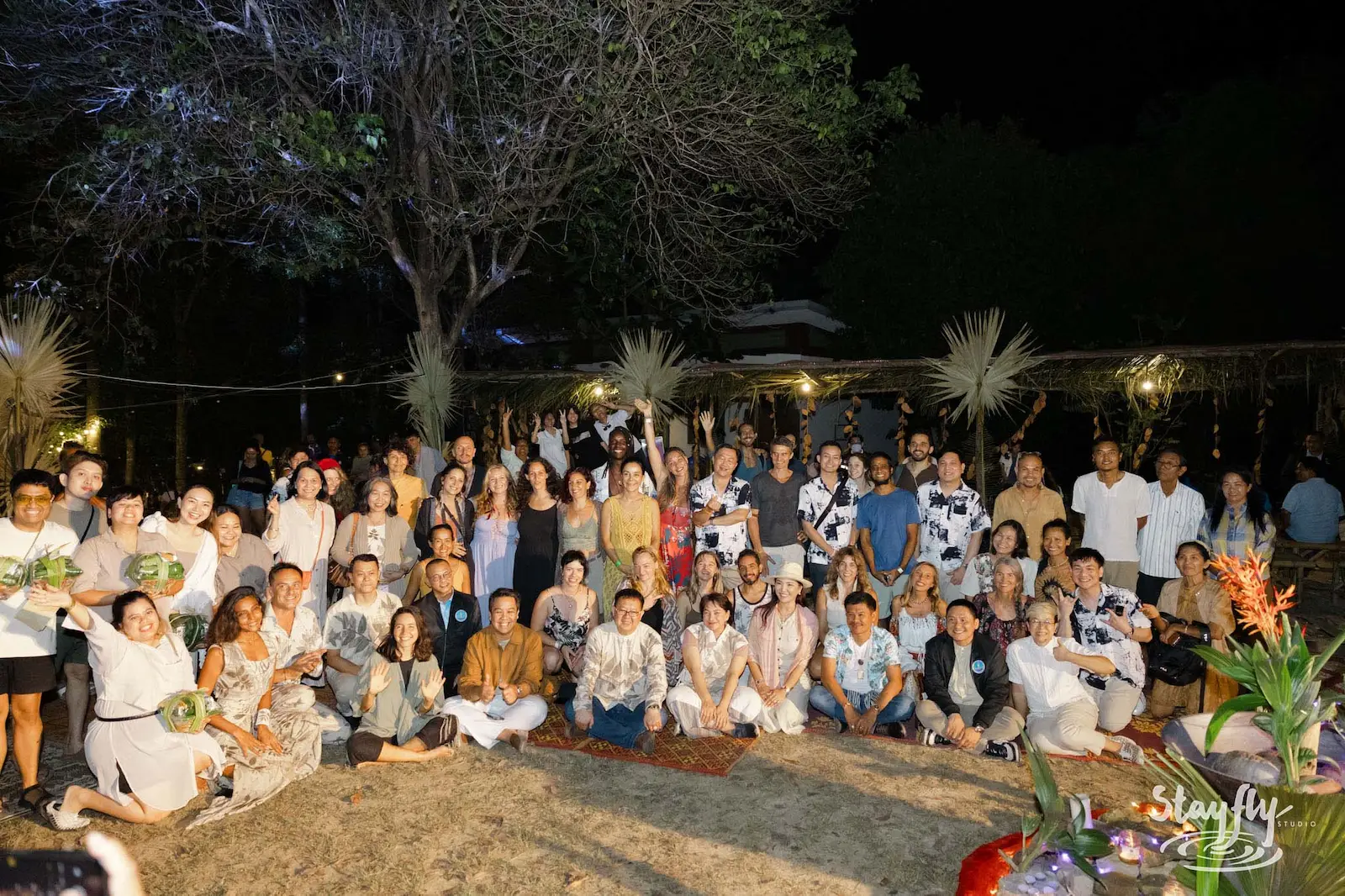 Large group posed together at night under tree.