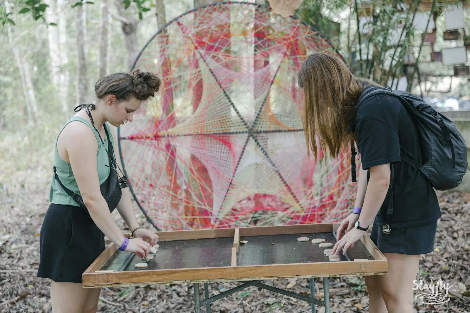 Two women playing a wooden game beside mandala art.