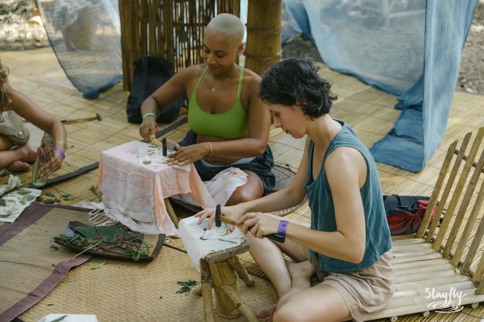 Two women carving at outdoor craft workshop table.