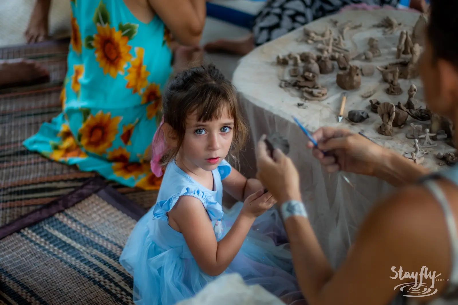Girl in blue dress at clay figure craft table.