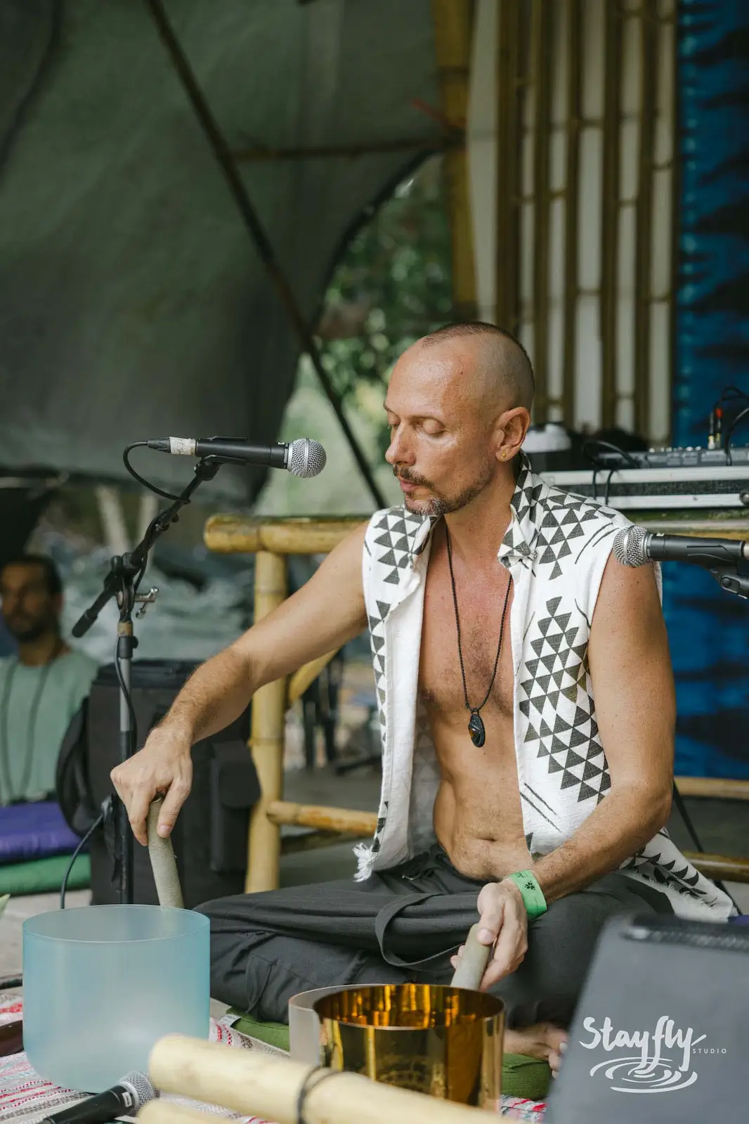 Man playing singing bowls seated at mic.