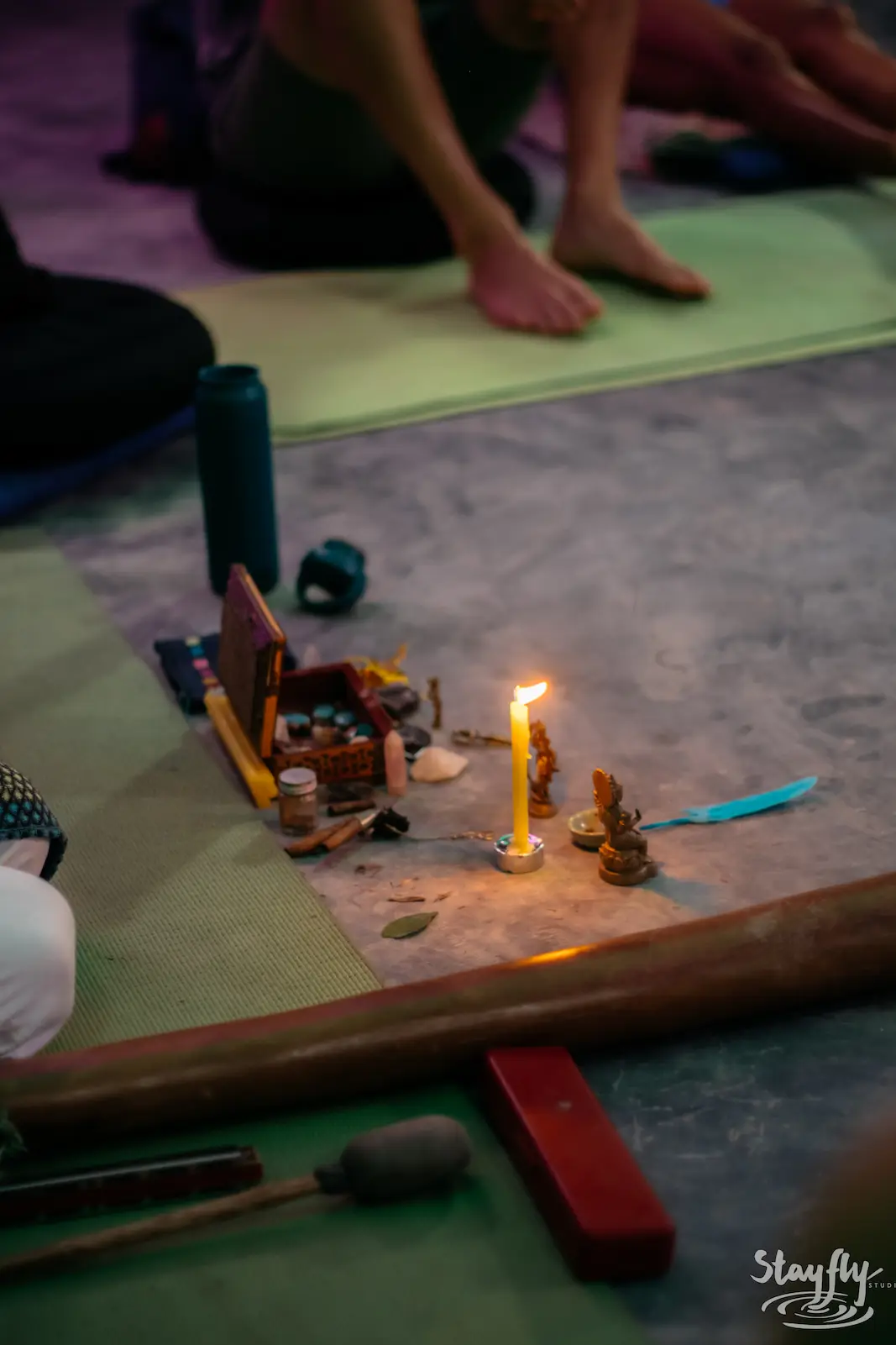 A candle and small instruments on the floor beside participants seated on mats.